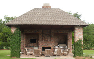 A full shot of an outdoor living area that includes chairs, an outdoor kitchen and fireplace.